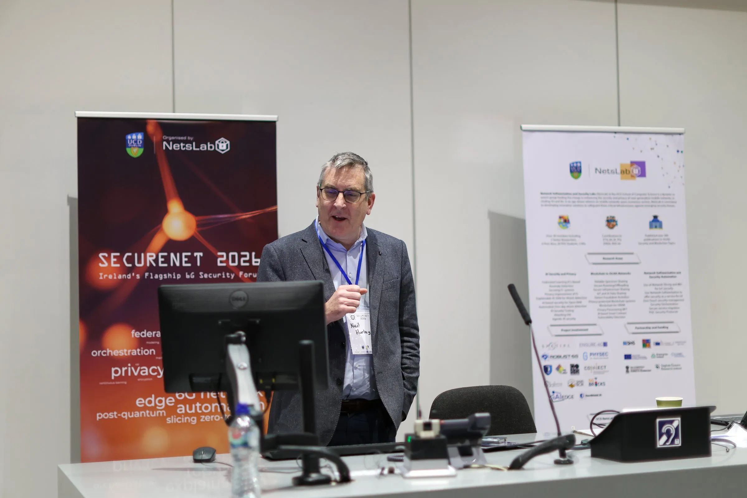 A talk at SECURENET 2026 in front of the event banners