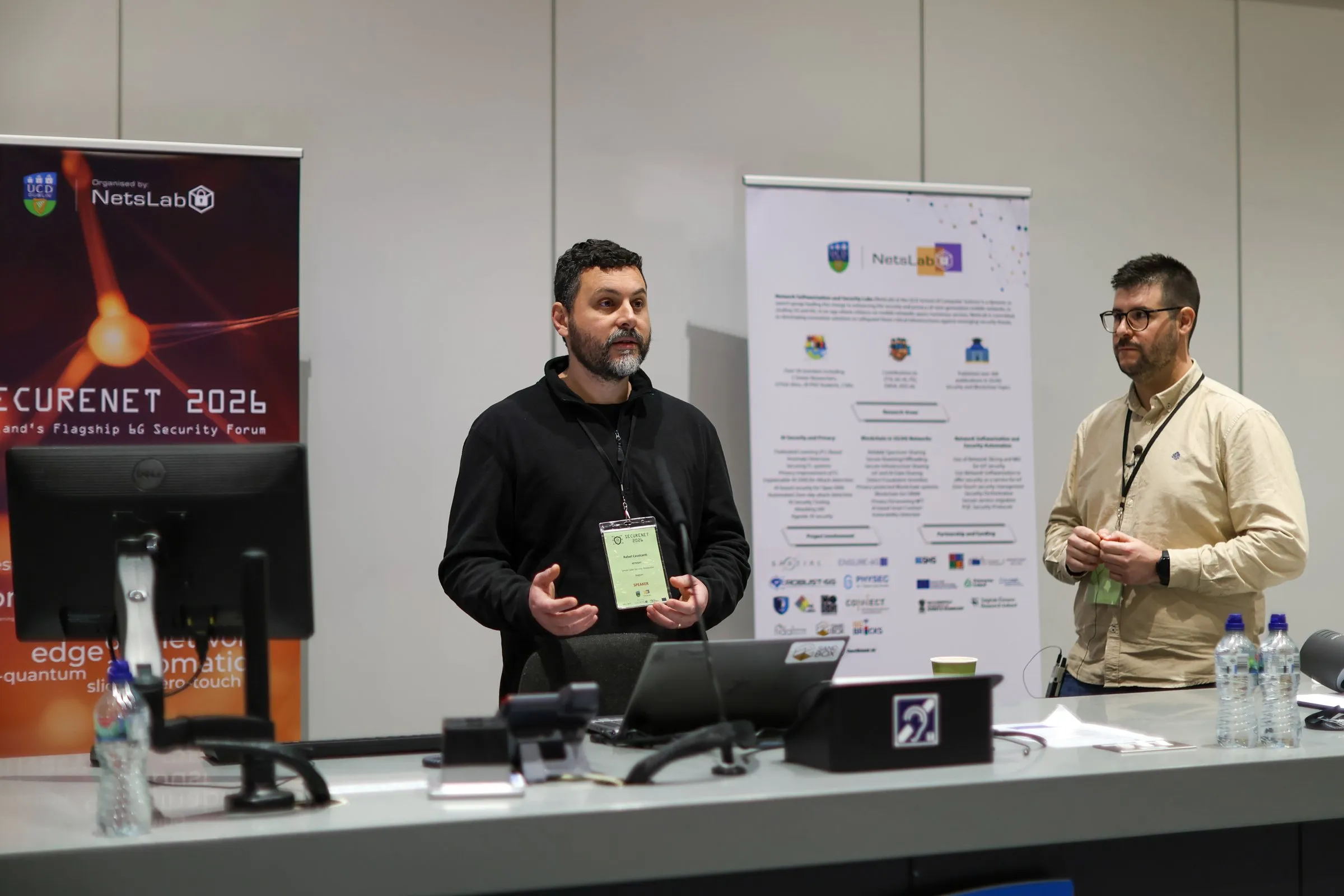 A speaker presenting at SECURENET 2026 beside a session moderator